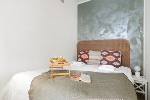 A bed with a woven headboard, a bedside table with a tray of breakfast, a book, and a patterned pillow. - Cozy & Stylish Downtown Studio for Four guests (Tampere)