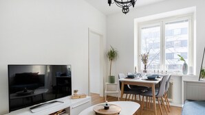 A modern living room with a flat-screen TV, a dining area with a table set for two, and a large window providing a view of the outside. - Cozy & Stylish Downtown Studio for Four guests (Tampere)