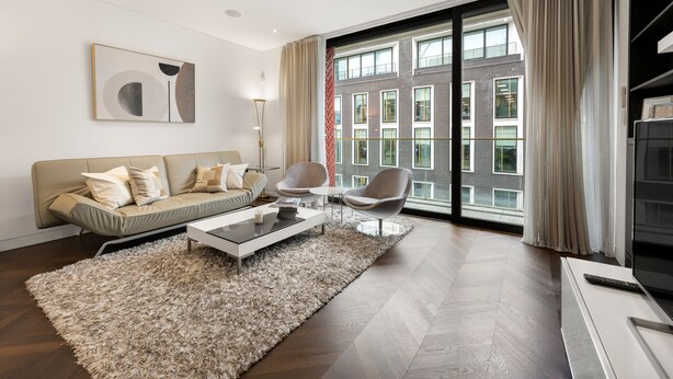 Un salon moderne avec un canapé, des fauteuils, une table basse et une grande fenêtre agrémentée de rideaux.