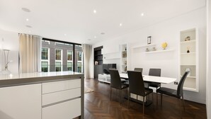 Une cuisine moderne avec un coin repas, des meubles blancs et un parquet disposé en motif à chevrons.