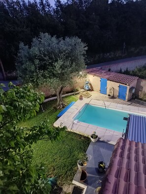 Una piscina, un pequeño edificio con puertas azules y un jardín.