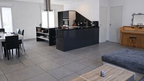 Moderni keittiö, jossa on keskeinen saareke, ruokailutila tuoleineen, sohva ja piano.