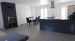 A modern kitchen with a central island, a dining area with a table and chairs, and a built-in TV.