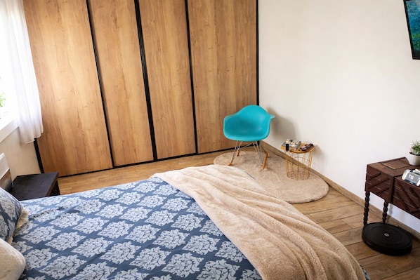 Une chambre à coucher avec un lit, une chaise bleue, une petite table et une armoire.