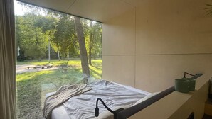 Een kamer met een bed, een raam met uitzicht op bomen en een groen voorwerp op het nachtkastje.