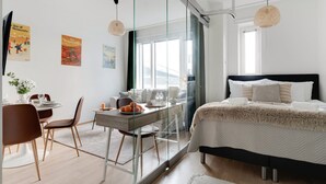 A modern hotel room with a bed, a desk, and a dining area.