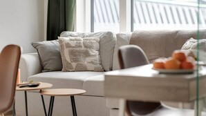 A modern living room with a sofa, a small table, and a view of a building through a window.