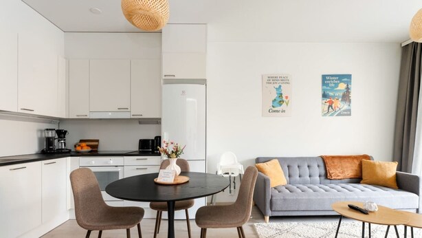 A modern living space with a dining area, kitchen, and a grey sofa with cushions.