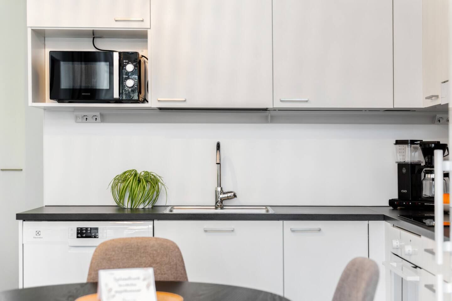 Une cuisine moderne avec des meubles blancs, un micro-ondes noir, une machine à café et un évier.