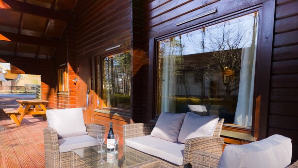 A wooden cabin with wicker furniture, large windows, and a wooden deck. - Tormore - wooden log cabin in the Cairngorms (Carrbridge)