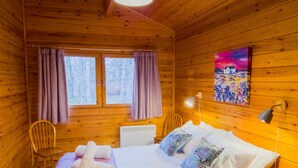 A wooden cabin room with a bed, two chairs, a table, a lamp, and a painting on the wall. - Tormore - wooden log cabin in the Cairngorms (Carrbridge)