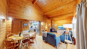 A wooden cabin interior with a dining area, kitchen, living room, and fireplace. - Tormore - wooden log cabin in the Cairngorms (Carrbridge)