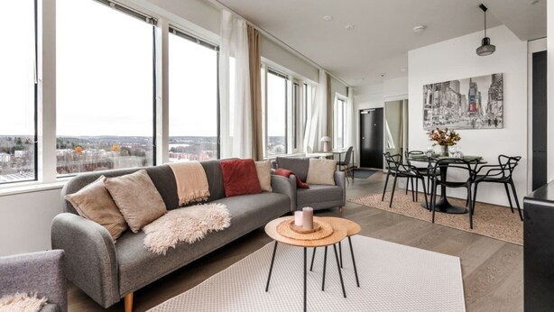 A modern living room with a sofa, a dining area, and large windows offering a city view.