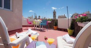 Terraza en la azotea con mobiliario exterior, una mesa y vistas a edificios históricos.