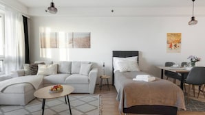 Una sala de estar moderna y bien iluminada, con un sofá, una mesa redonda, una cama con cabecera y un comedor con mesa y sillas.