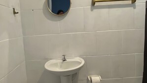 A bathroom with white tiled walls, a pedestal sink, a small mirror, a towel rack, and a toilet.