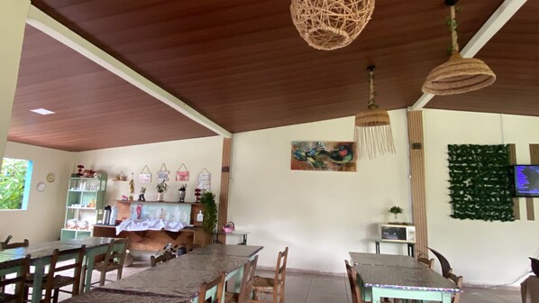 Ein Essbereich mit Holztischen und -stühlen, einer hängenden Lampenschirm aus Bändern, einem Wandbild und einem Fernseher.