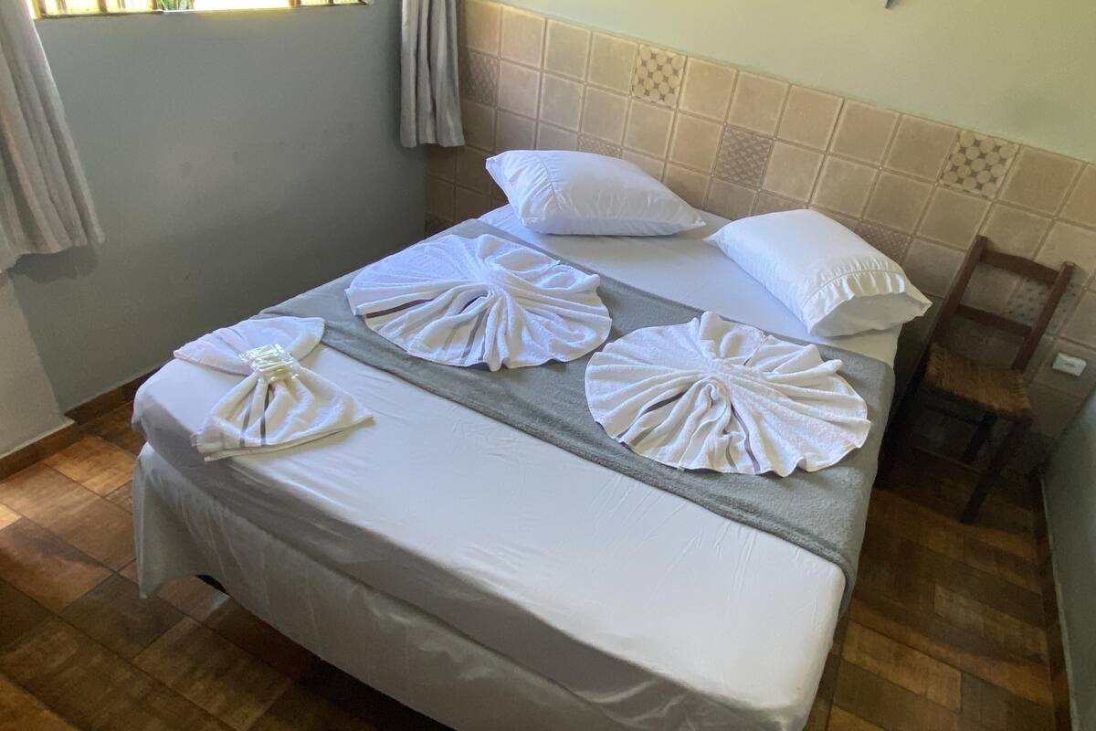 A neatly made bed with white linens and towels arranged in a fan shape, a headboard with a patterned tile design, and a wooden floor.