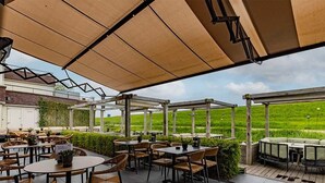 Un patio al aire libre con mesas y sillas, un área techada y vistas a un campo verde.