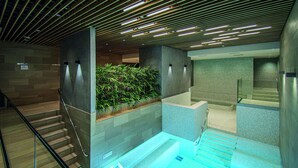 Un área de piscina interior moderna con barandilla de vidrio, techo de madera y pared verde con plantas.