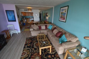 Ein Wohnzimmer mit einem beigen Sofa, einem Glastisch und einem Teppich mit Muster.