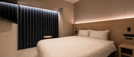 Una habitación de hotel con una cama grande, una mesita de noche, un televisor montado en la pared y una ventana con cortinas.