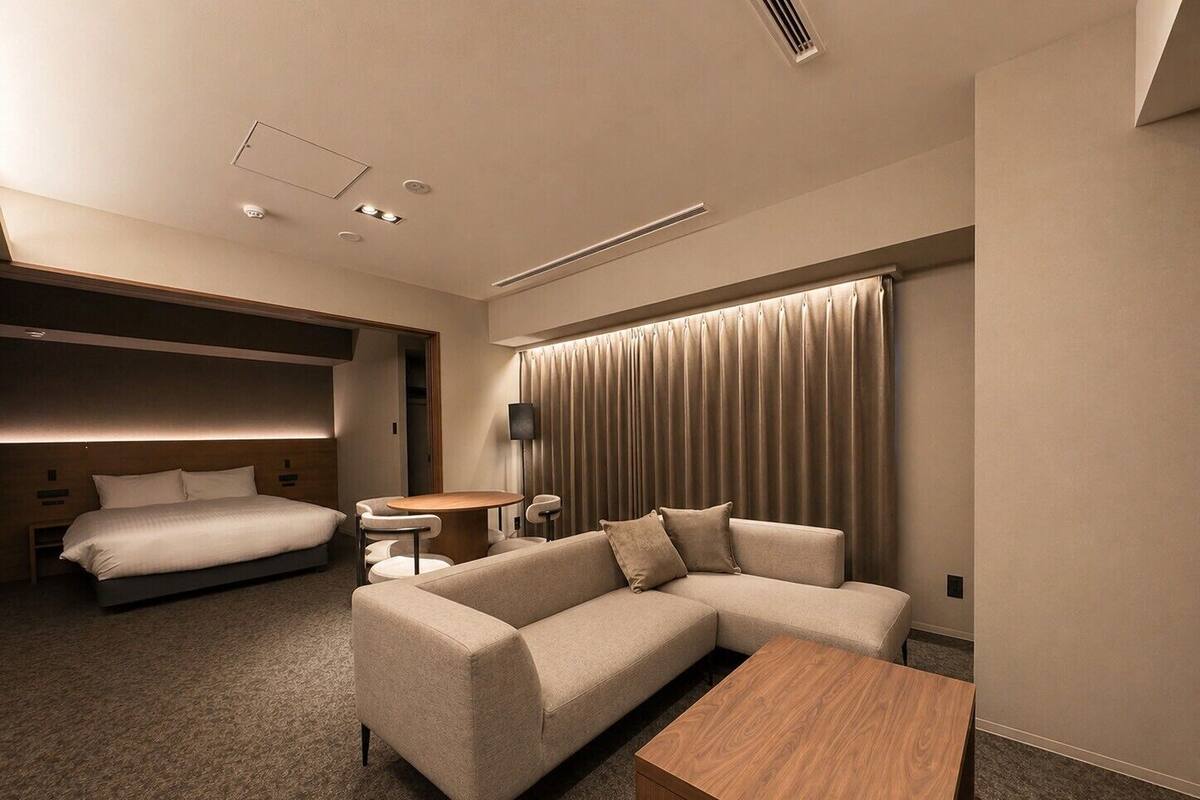 A modern hotel room with a bed, sofa, and a small table.