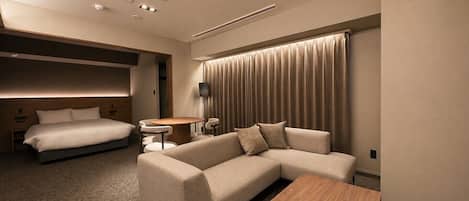 A modern hotel room with a bed, sofa, and a small table.