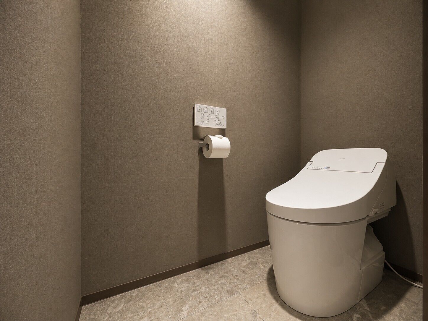 Un baño moderno con inodoro, dispensador de toallas de papel en la pared y botón de descarga.