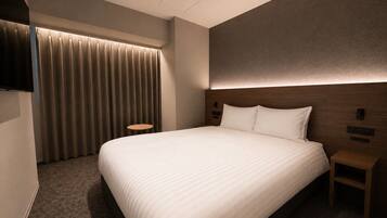 A hotel room with a large bed, a TV mounted on the wall, a bedside table, and a curtain.