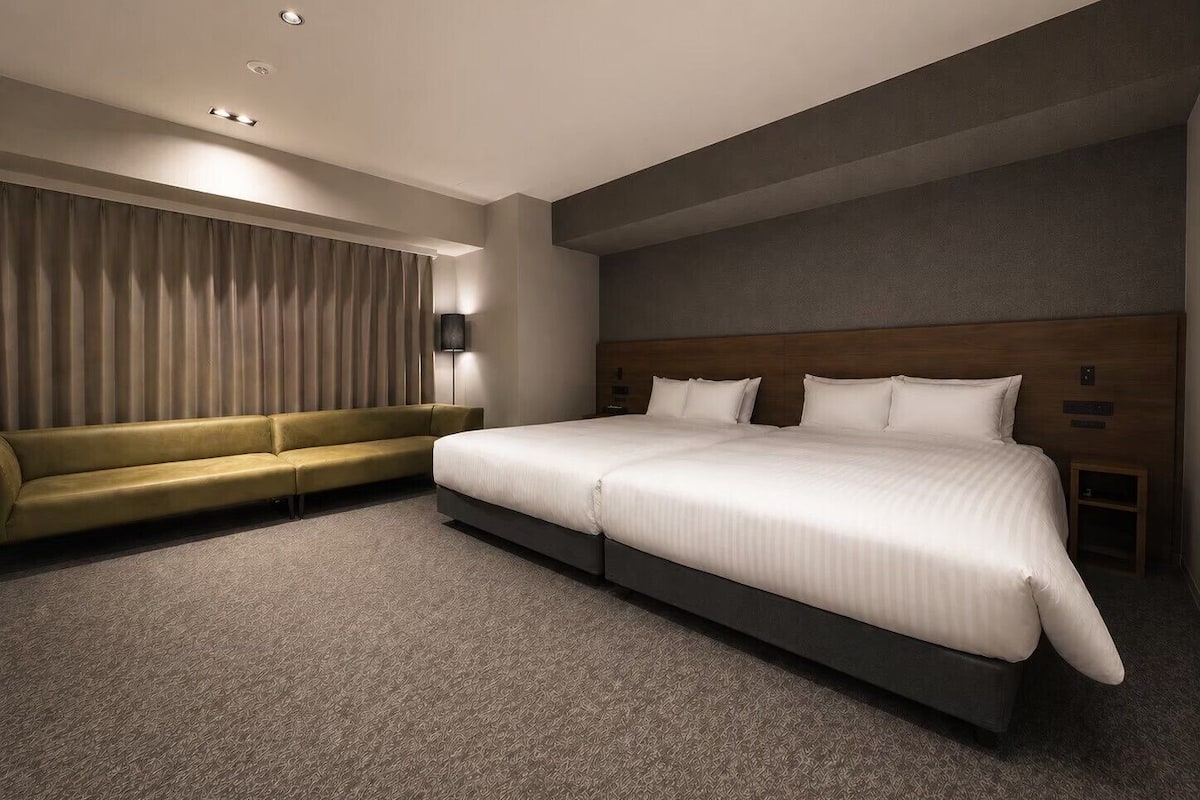 A modern hotel room with a large bed, a sofa, a lamp, and a wall-mounted TV.