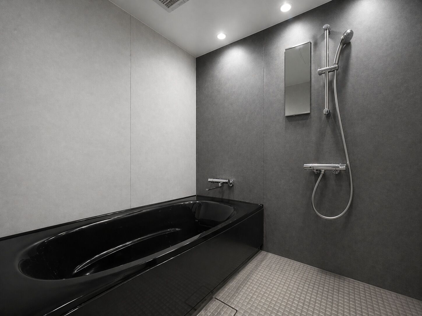 A modern bathroom with a black bathtub, a handheld showerhead, and a wall-mounted mirror.