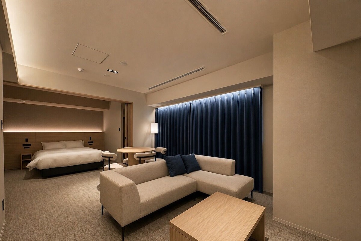 A modern hotel room with a bed, sofa, coffee table, and a small dining table.