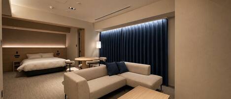 A modern hotel room with a bed, sofa, coffee table, and a small dining table.