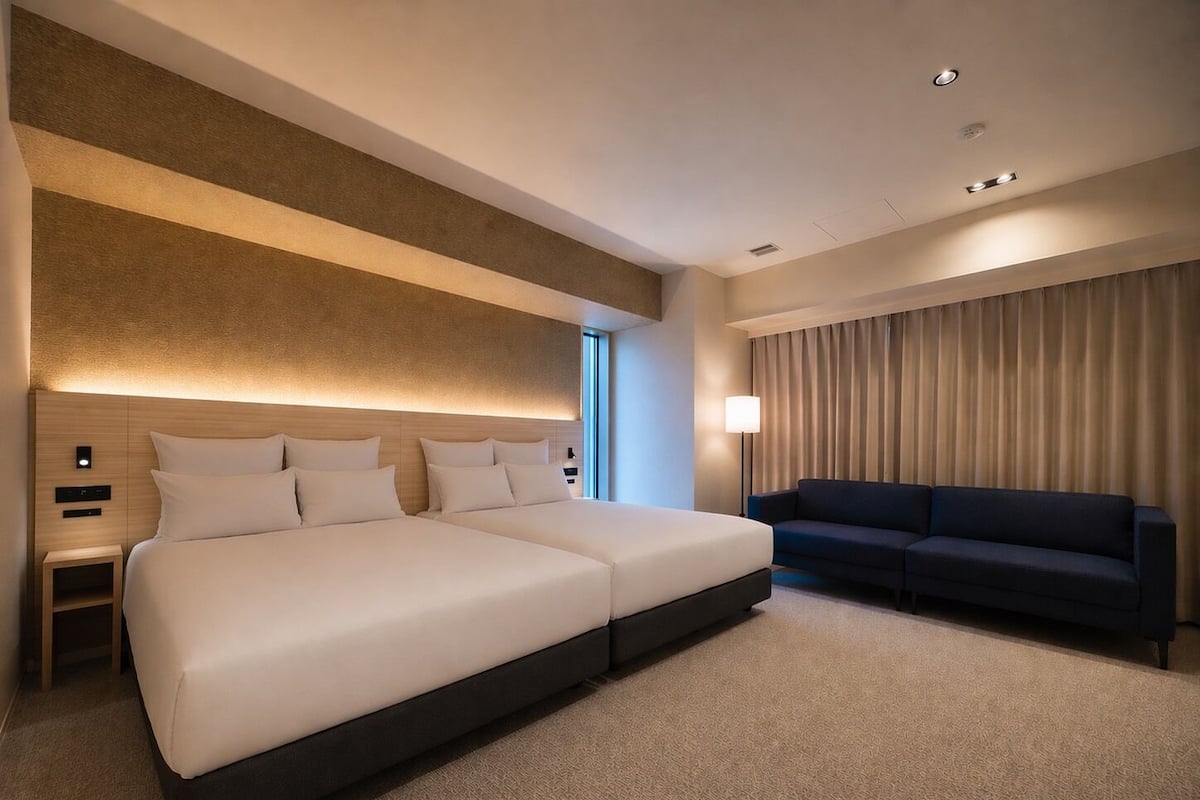 A modern hotel room with a large bed, a sofa, a nightstand, and a lamp.
