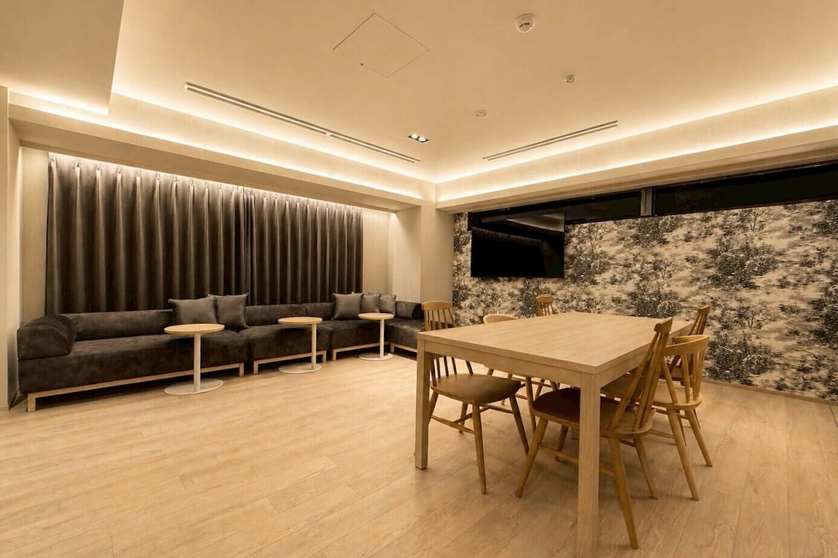 A modern living room with a sofa, a dining table, and a TV mounted on the wall.