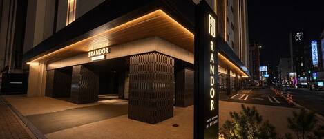 Entrada de un hotel con fachada moderna, un letrero que dice 'RANDOR Heritage' y un camino bien iluminado que conduce a la entrada.