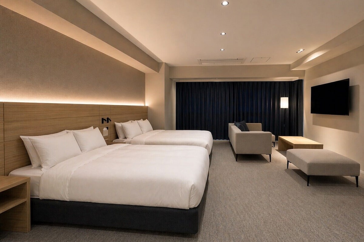 A hotel room with two beds, a sofa, a TV, and a desk.