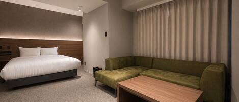 A modern hotel room with a bed, a green sofa, a wooden coffee table, and a large window with curtains.