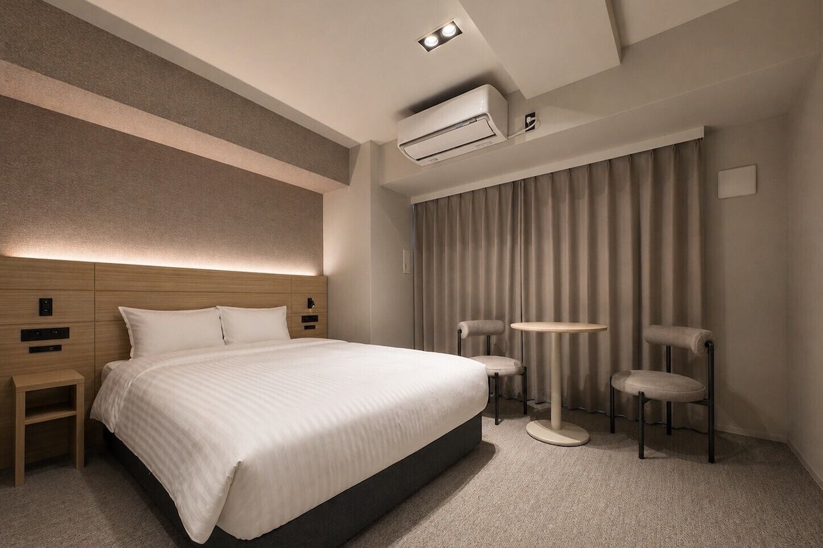 A modern hotel room with a large bed, bedside tables, a round table, and a chair.