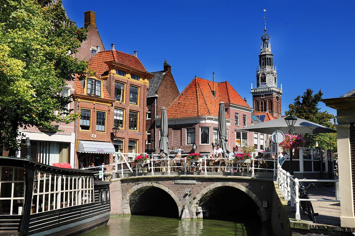 A canal bridge with buildings, a boat, and a tower.