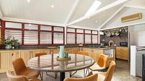 A modern kitchen with a round dining table, wooden cabinets, and a built-in oven. - Sea Light – the ultimate waterfront retreat (Currarong)