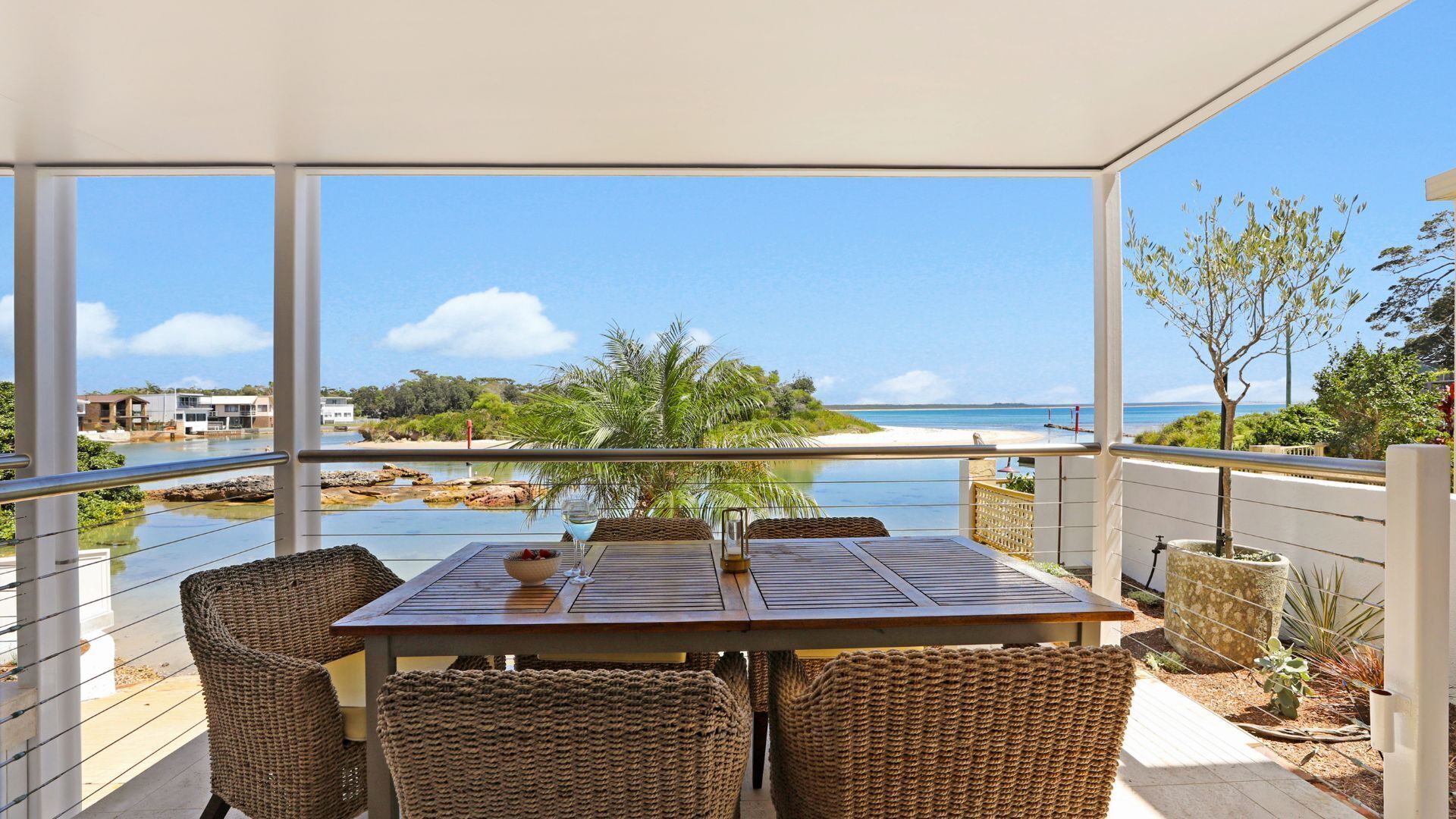 En balkon med et bord og stole, der vender ud mod en strand og vand.