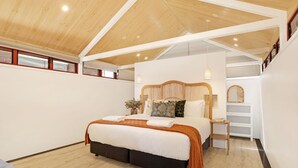 Un dormitorio con techo de madera, cama con ropa de cama blanca, mesita de noche y un espejo en la pared.