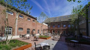 A courtyard with outdoor seating, brick buildings, and trees. - Discover Alkmaar from Unique Cell Room (Alkmaar)