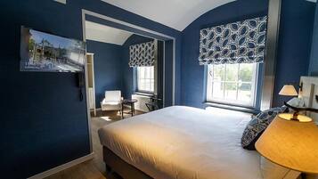 Ein Hotelzimmer mit Bett, Schreibtisch, Stuhl und einem Fenster mit gemusterten Vorhängen.