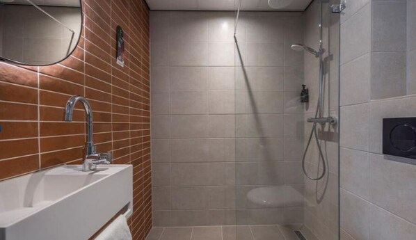 A modern bathroom with a white sink, a mirror, a shower, and a toilet.