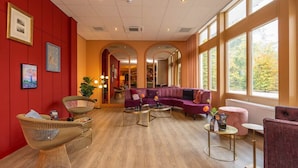 A hotel lobby with a wooden floor, red walls, and a purple sofa. There are wicker chairs and a small table with a vase. - Peaceful Forest Retreat with Bike Rentals, Breakfast, Terrace, and Free Parking (Vierhouten)