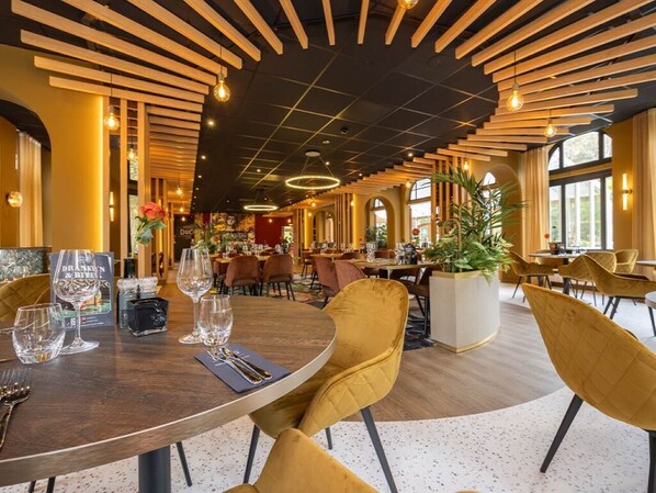 A restaurant with round tables, yellow chairs, and a modern ceiling design.
