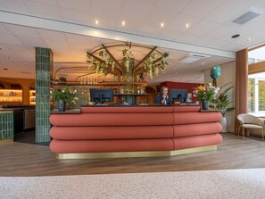 A reception desk with a modern design, a bar area in the background, and a large window providing natural light. - Explore Veluwe from Cozy Lodge: Bike Rentals,  Free Parking, Breakfast (Vierhouten)